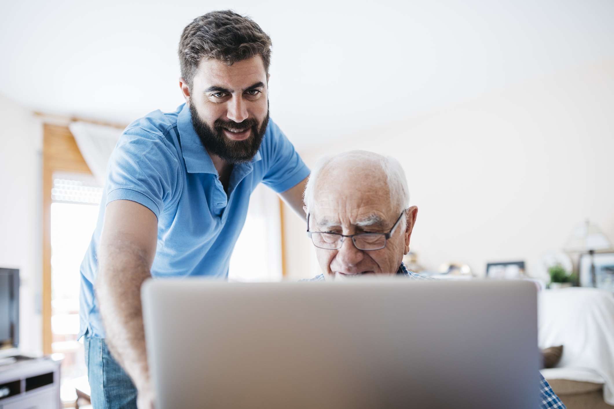 Een jongere volwassene helpt een oudere volwassene achter de computer. 