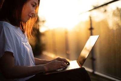Een vrouw die buiten in gedempt licht naar haar laptop kijkt