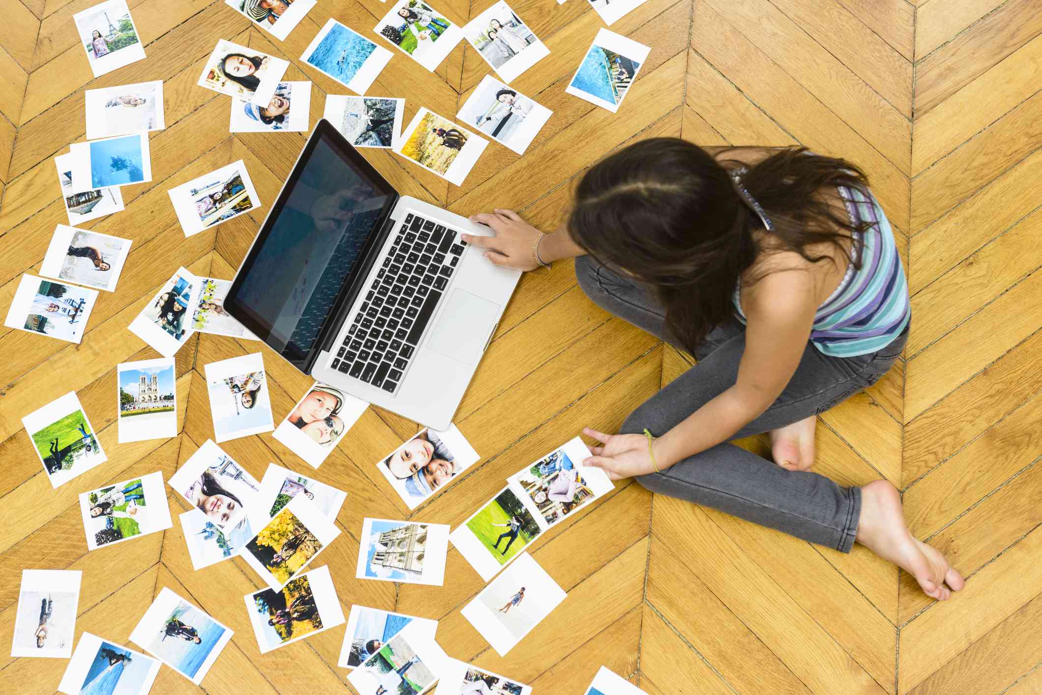 Iemand die op de grond zit te kijken naar foto's op een laptop met overal foto's.