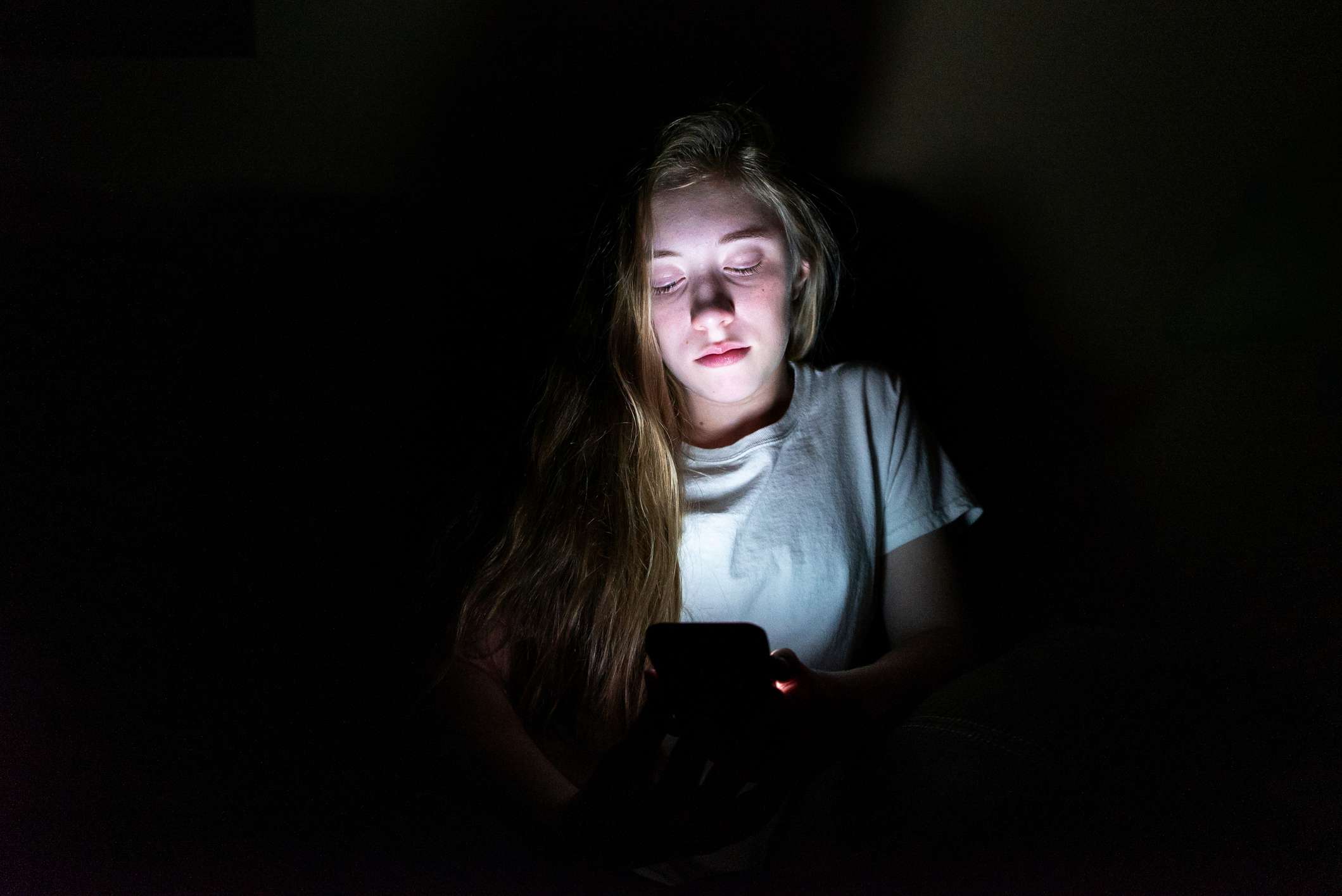 Een tiener die in het donker een smartphone gebruikt. 