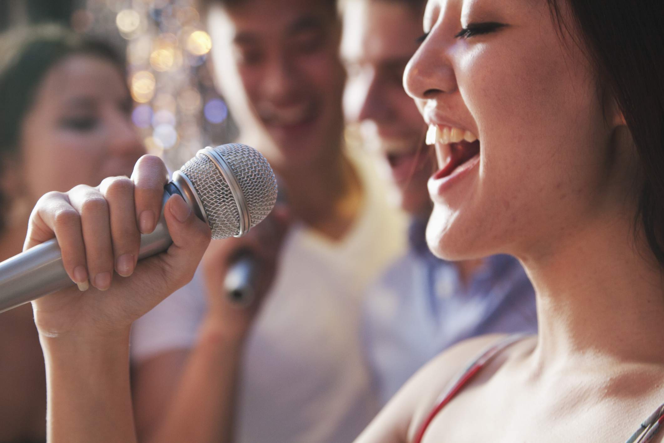 Een close-up van een vrouw die in een microfoon zingt met vrienden op de achtergrond