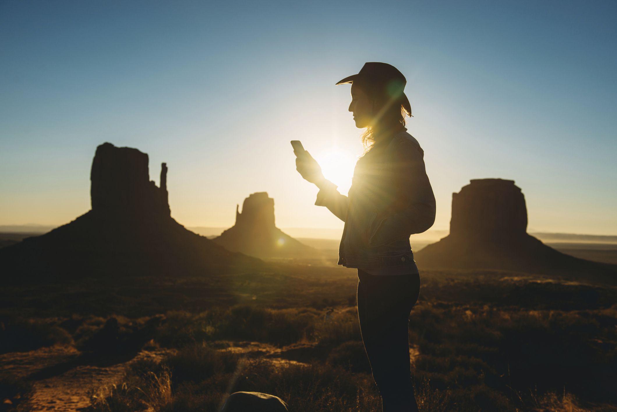 Iemand die bij zonsopgang een smartphone gebruikt in Monument Valley, Utah. 