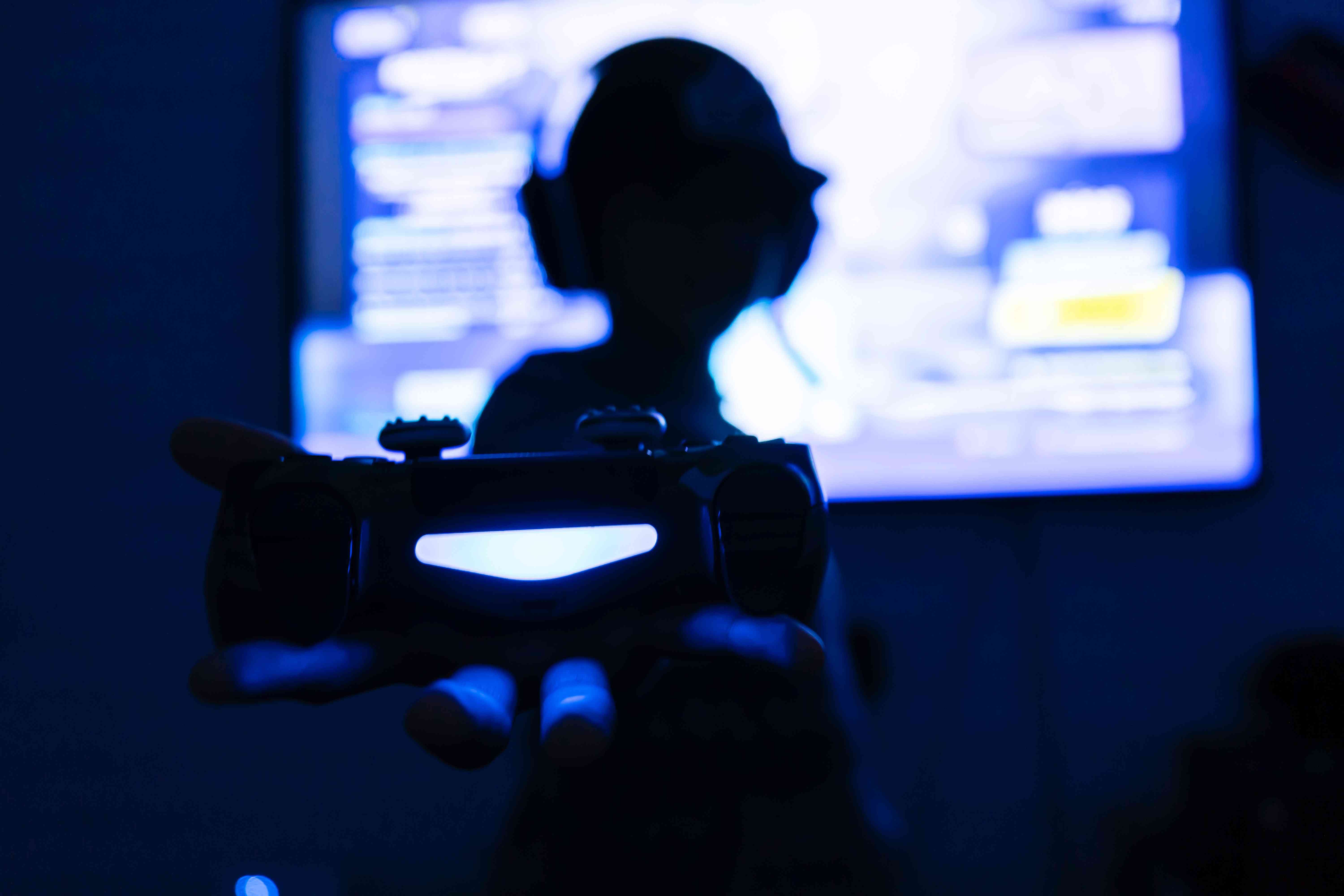 Silhouet van een gaming-streaming die een gamecontroller vasthoudt met een game op het scherm erachter.