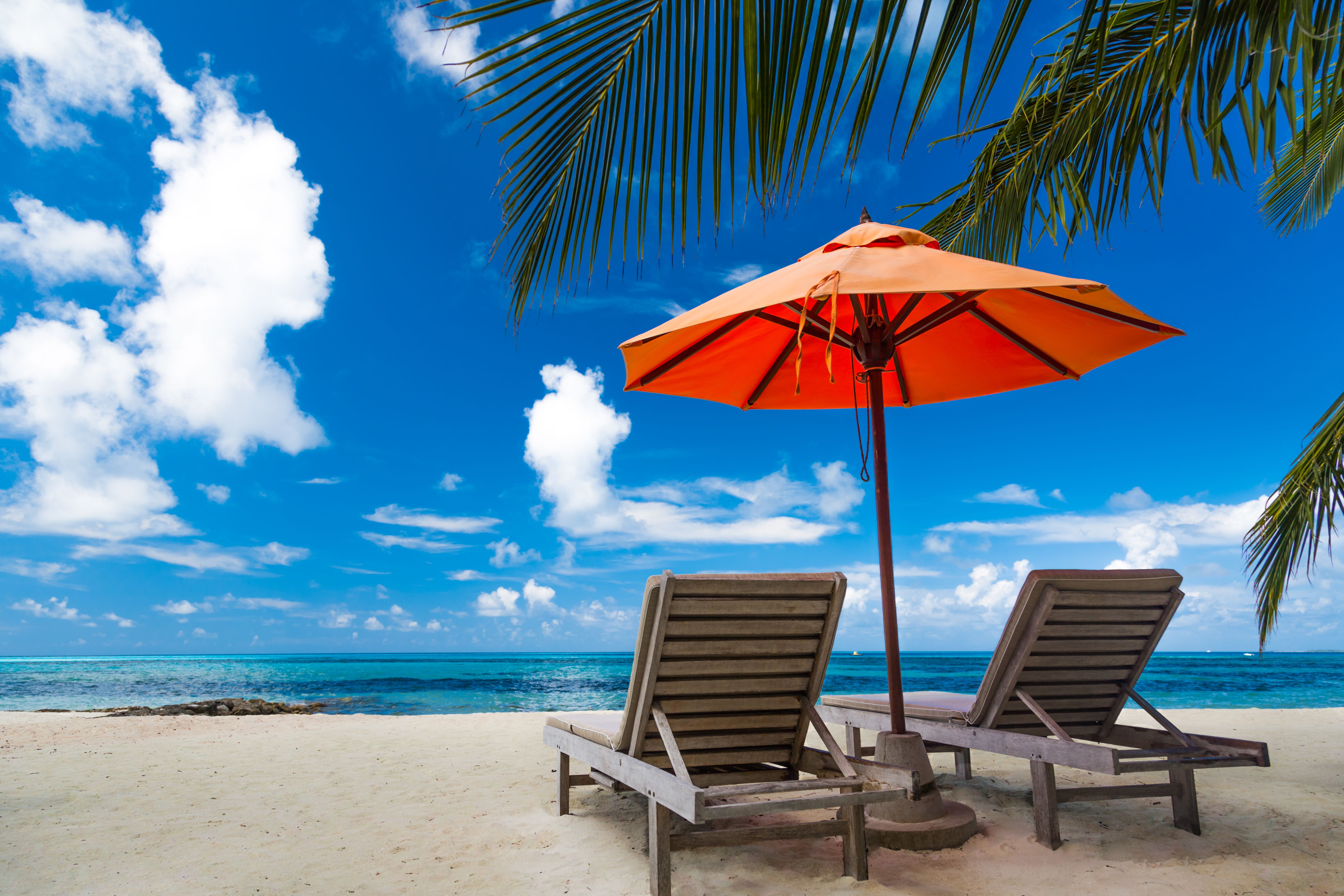 Mooie strandachtergrond voor de zomerreis met zon, kokosnootboom en strand houten bed op zand met mooie blauwe zee en blauwe hemel.  Zomer stemming zon strand achtergrond concept.