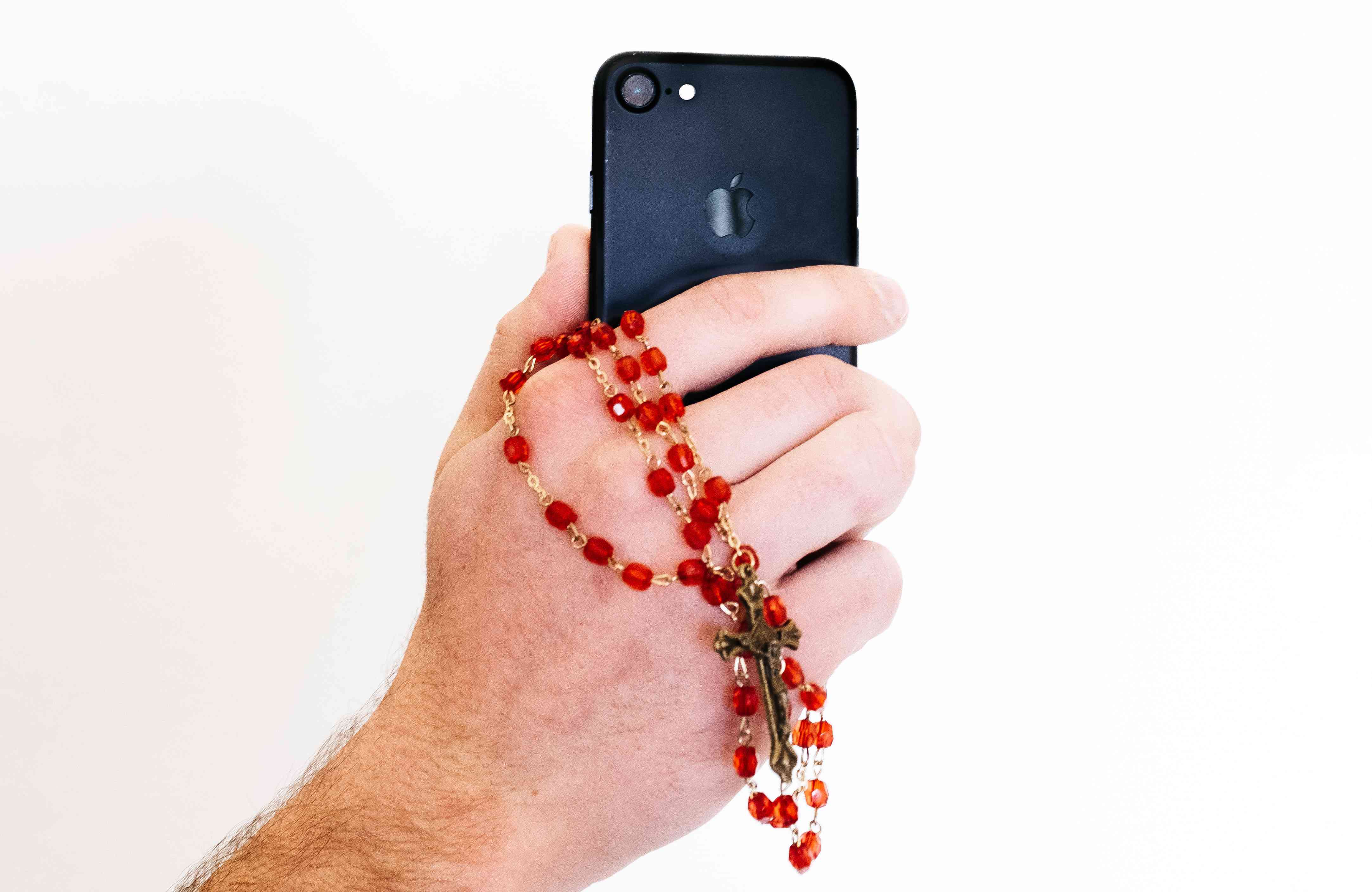 Een close-up van een hand met een smartphone en een rozenkrans.