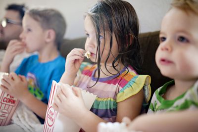 Een vader en zijn kinderen kijken films op de bank terwijl ze popcorn eten.