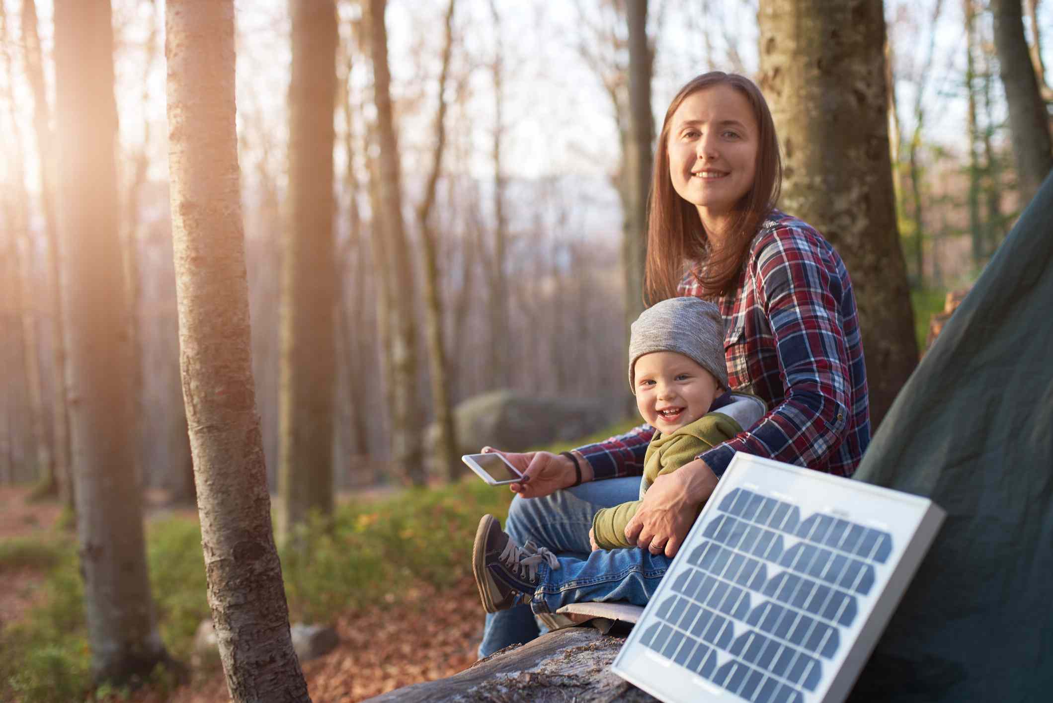 Een jonge ouder en kind in de buurt van een tent in het bos met een zonnepaneel dat energie verzamelt van sunling.