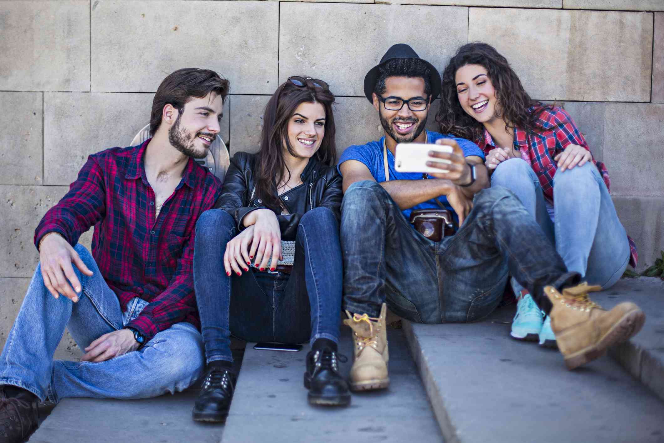 Vier vrienden kijken naar een film op een smartphone die buiten op een betonnen trap zit.
