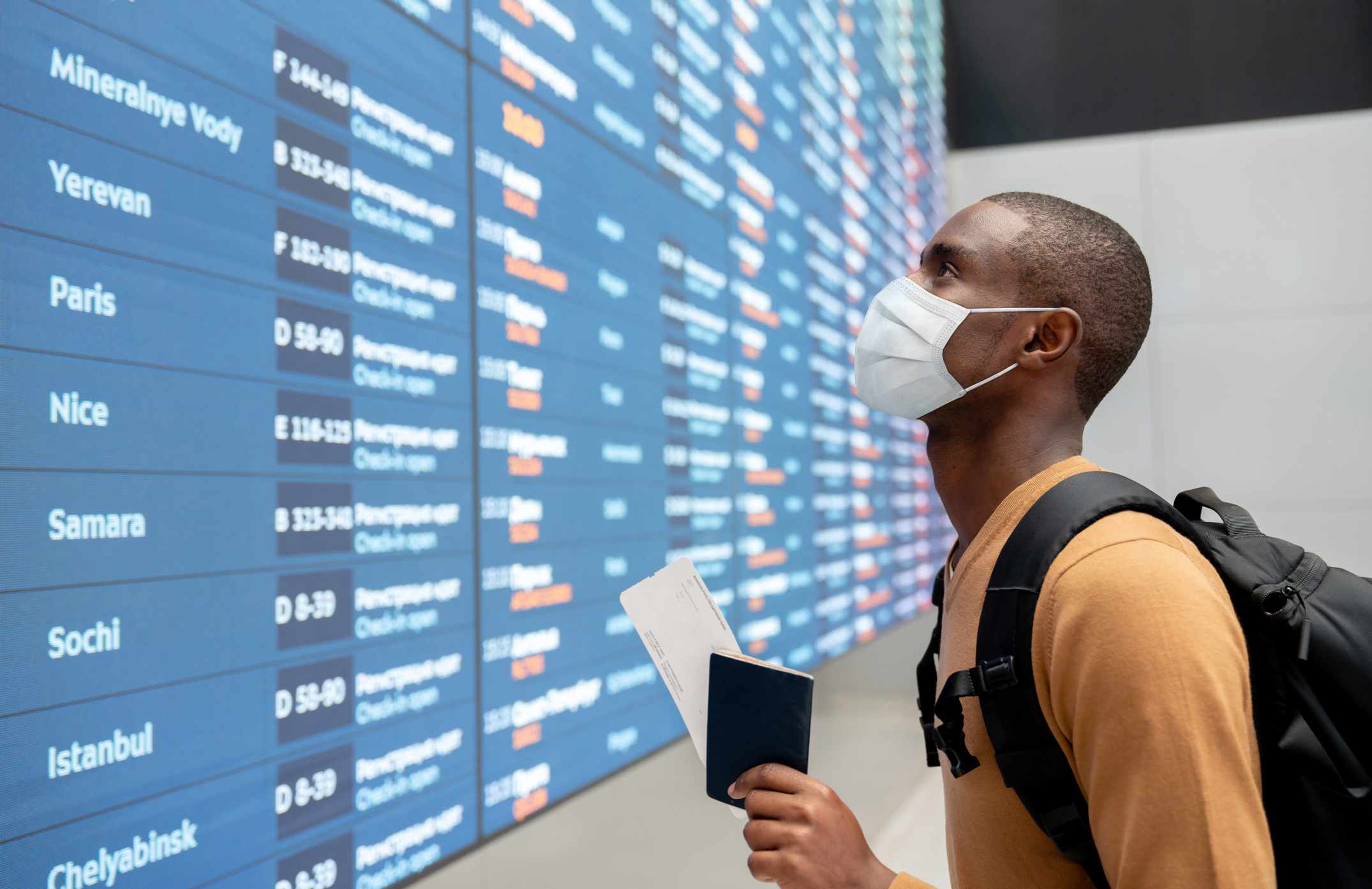 Reiziger die een gezichtsmasker draagt ​​op de luchthaven en naar het vluchtschema kijkt.