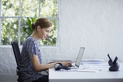 Een zijaanzicht van een vrouw die achter haar bureau zit te typen op een laptop