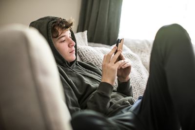 Een tiener die op een bank zit en aandachtig naar zijn smartphone kijkt