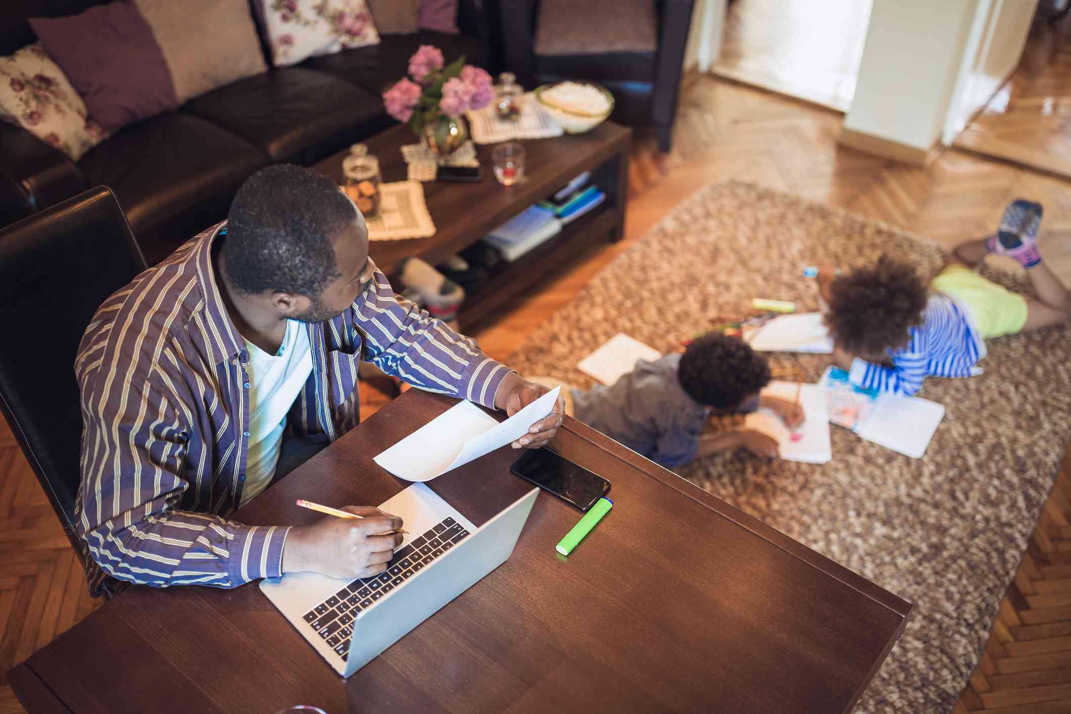 Vader werkt thuis terwijl zijn twee kinderen in de woonkamer spelen