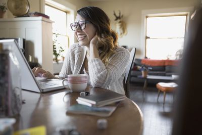 Lachende vrouw met laptop aan keukentafel