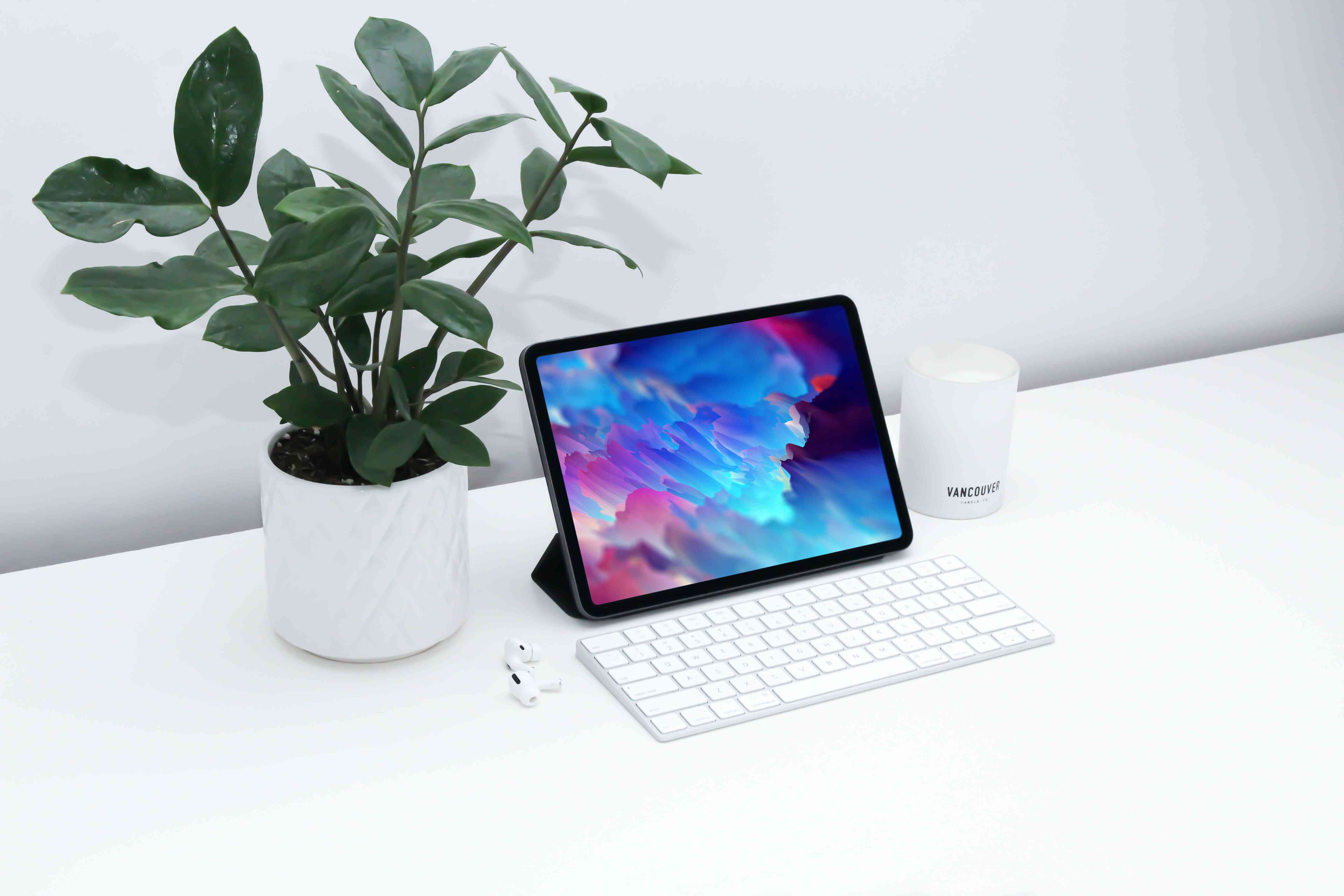 Een iPad in een opgevouwen standaardbehuizing met een toetsenbord ervoor op een wit bureau. 