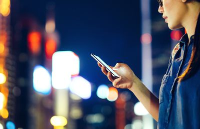Een vrouw op een straat in de stad 's nachts kijken naar haar smartphone.