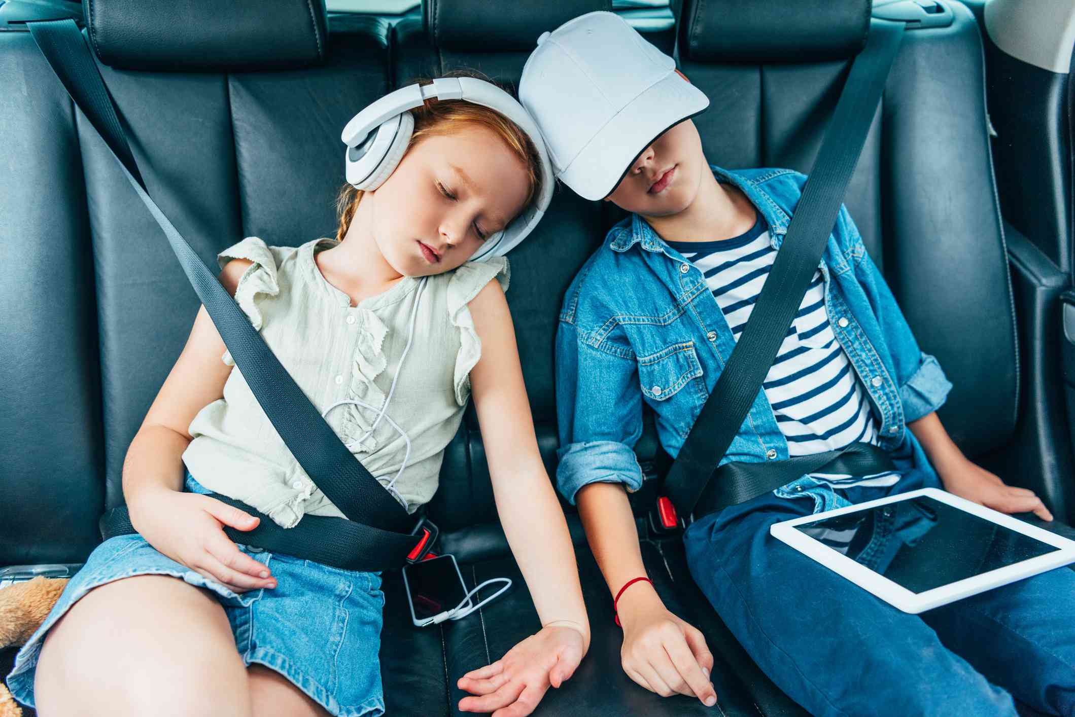 Twee kinderen slapen in de auto met elektronische apparaten die voor schoolwerk kunnen worden gebruikt. 