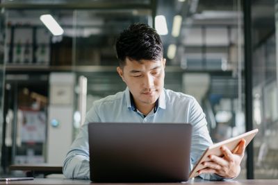 Een man die aan een bureau zit en tegelijkertijd naar een laptop en tablet kijkt