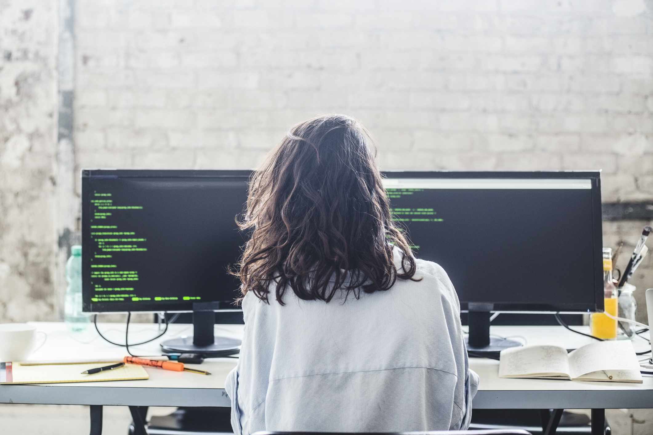 Achteraanzicht van vrouwelijke computerhackercodering aan bureau in creatief kantoor