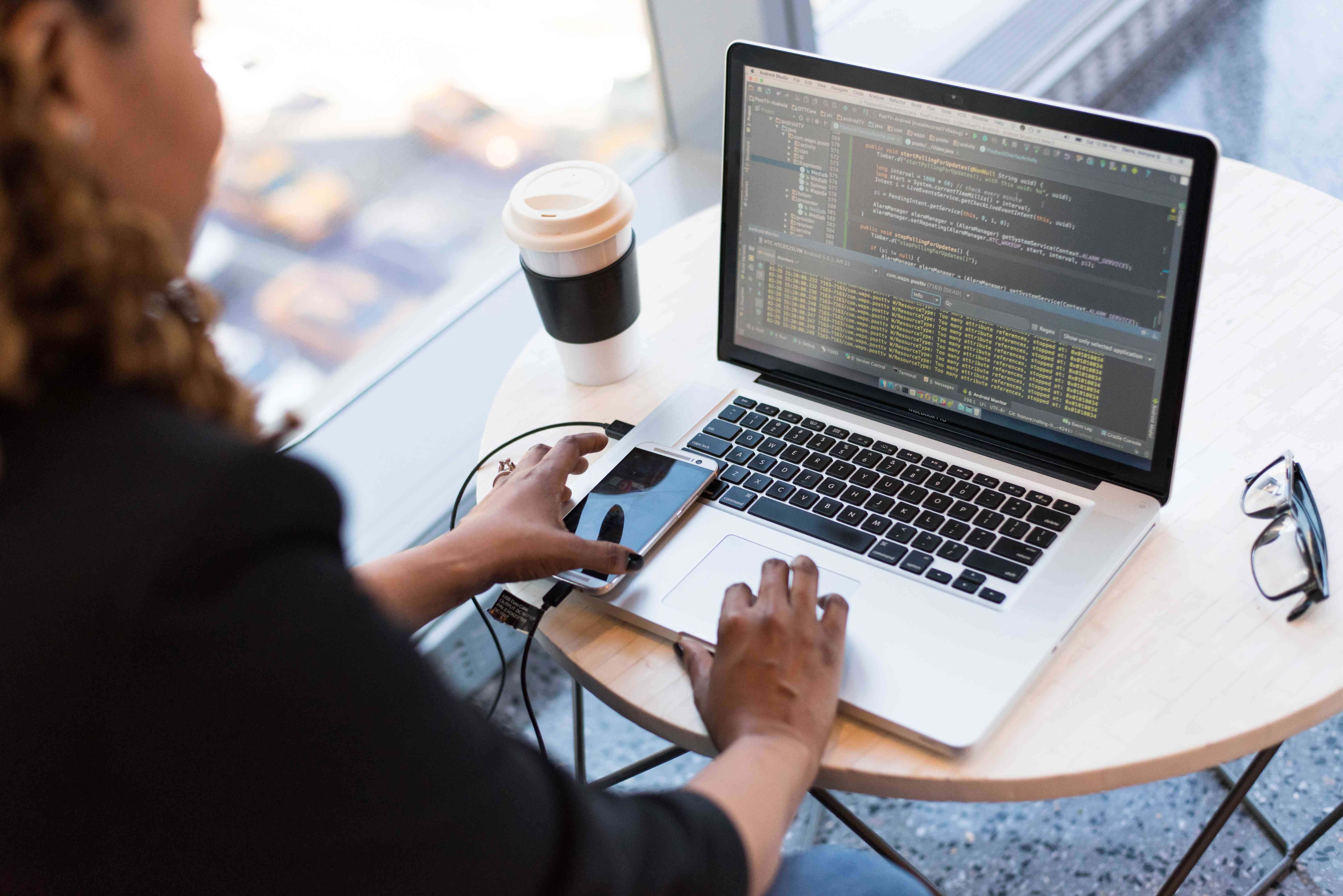 Een app-ontwikkelaar die op een laptop werkt met een smartphone die via een kabel is verbonden.