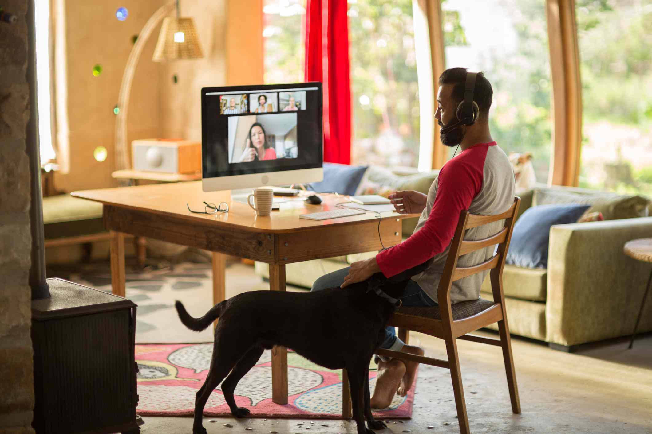 Man werkt vanuit huis op zijn computer en aait zijn hond tijdens lockdown