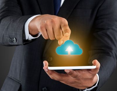 Een foto-illustratie die een man toont die een smartphone vasthoudt terwijl een tekening van een wolk bedoeld is om gegevens weer te geven die van de telefoon naar externe opslag worden geüpload.