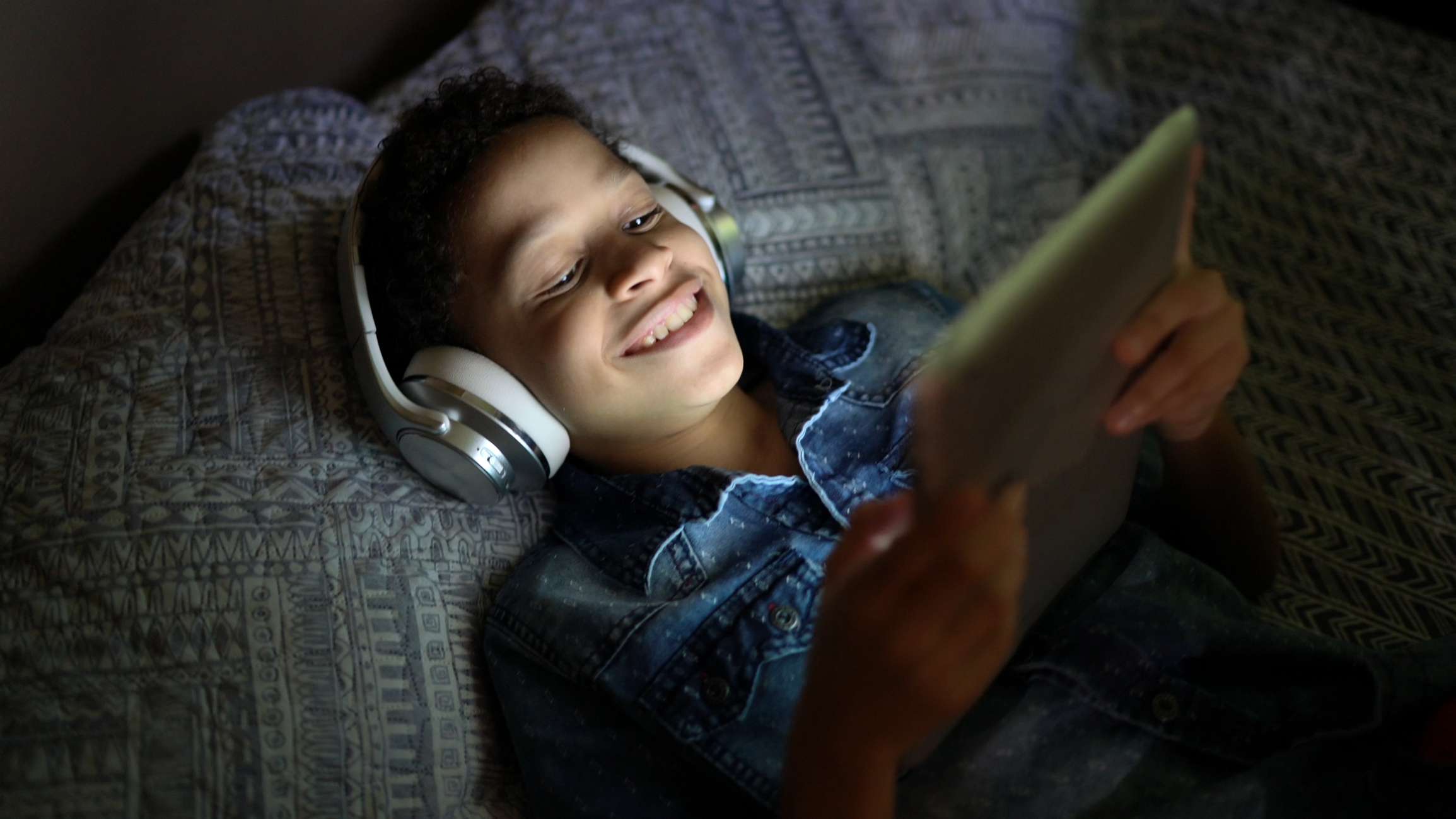 Een tiener die in bed ligt en een film kijkt op een tablet. 