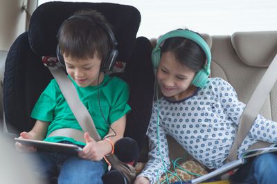 Kind speelt spel op tablet in auto terwijl zus toekijkt