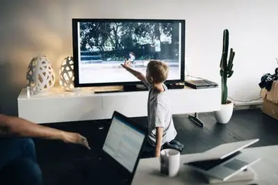 Een jonge jongen die een tv-scherm aanraakt waarop een digitale foto wordt gecast vanaf een laptop via chromecast.