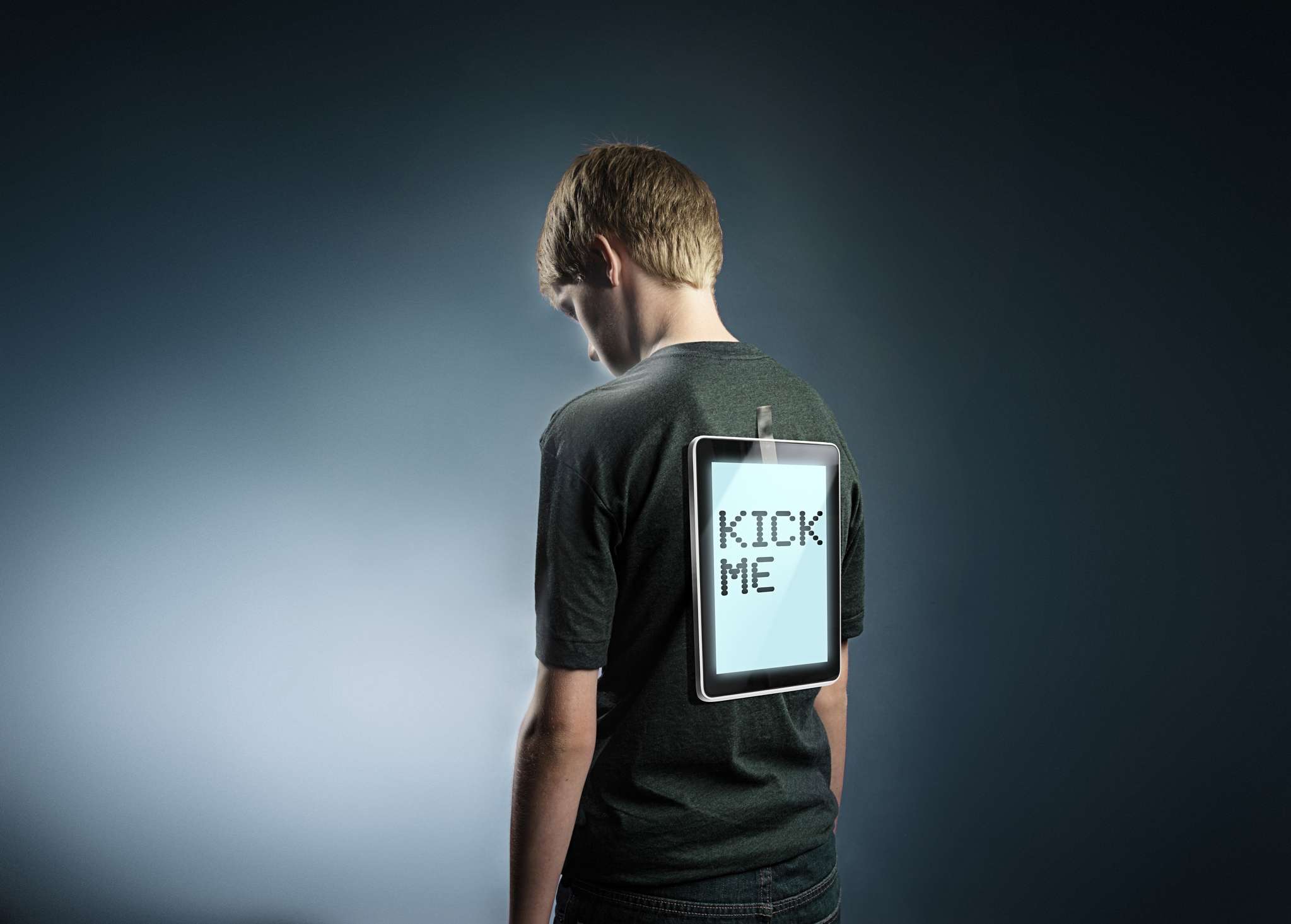 Een jonge tiener met een tablet op hun rug geplakt met de tekst "Kick me", om cyberpesten te vertegenwoordigen.