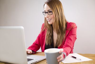 Vrouw die aan laptop werkt die koffiemok houdt.