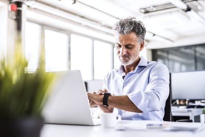 Volwassen zakenman zit aan bureau in kantoor kijken naar smartwatch