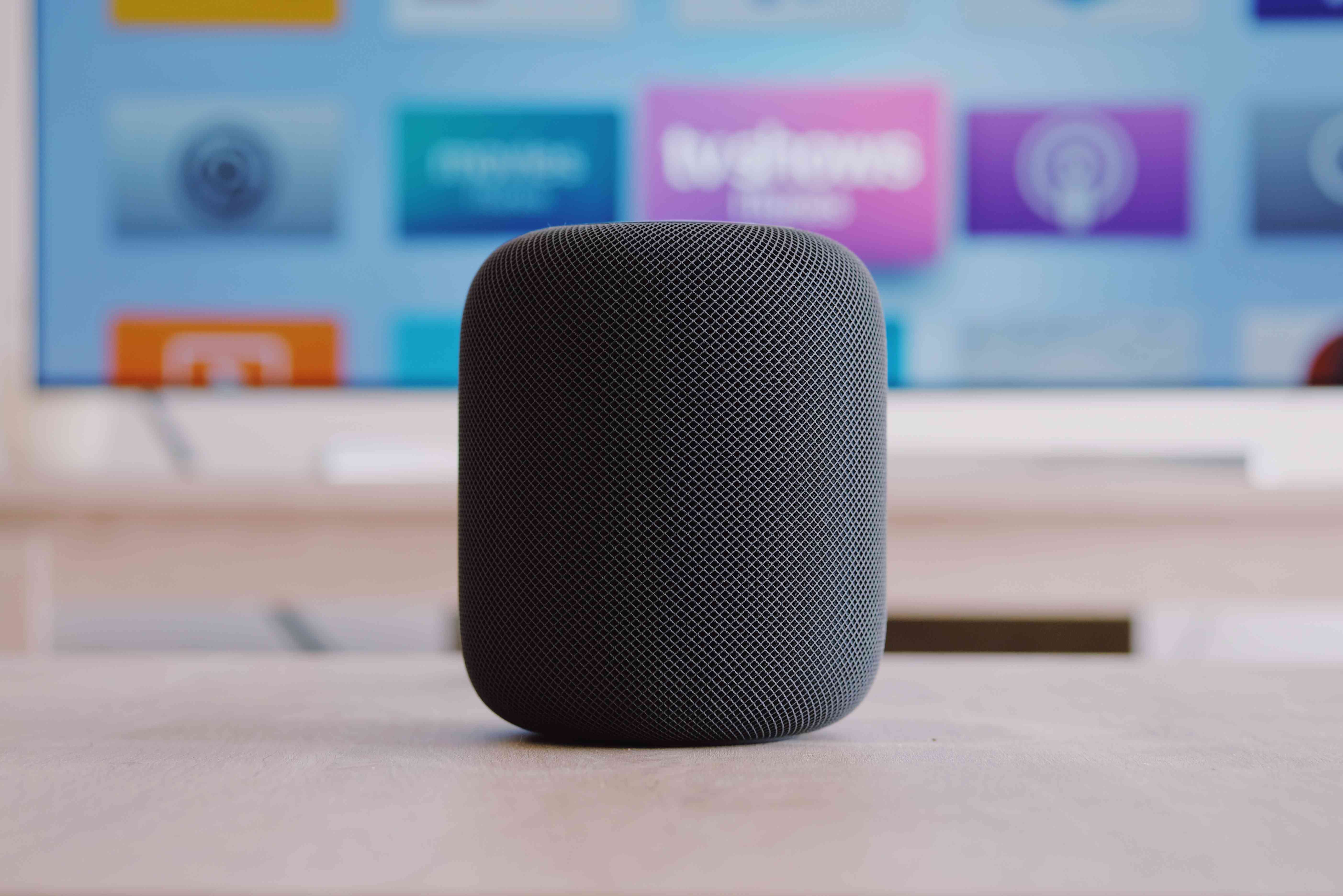 Een Apple Homepod met een televisie op de achtergrond.