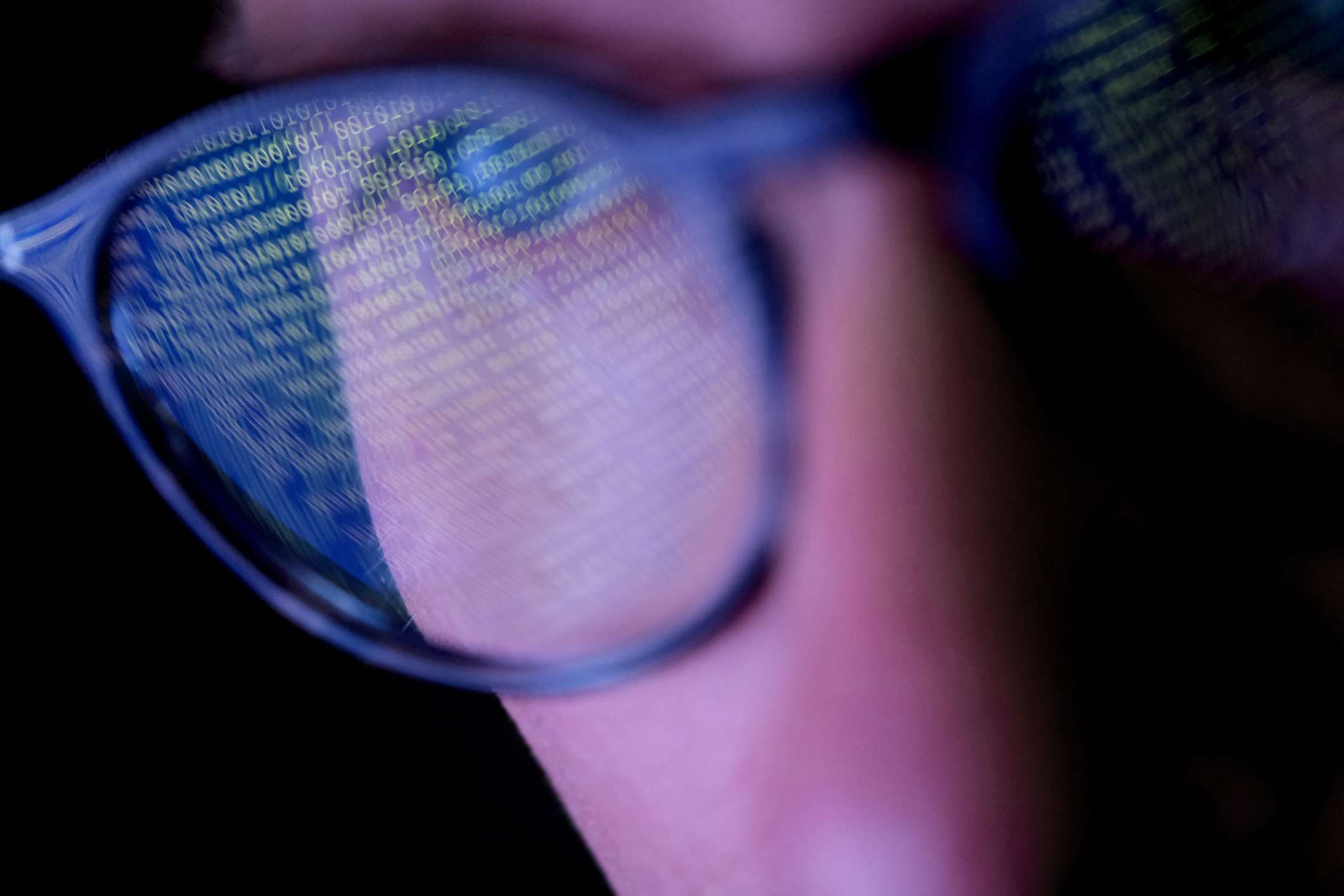 Een close-up van iemand die een bril draagt ​​met binaire code die reflecteert op de lenzen. 