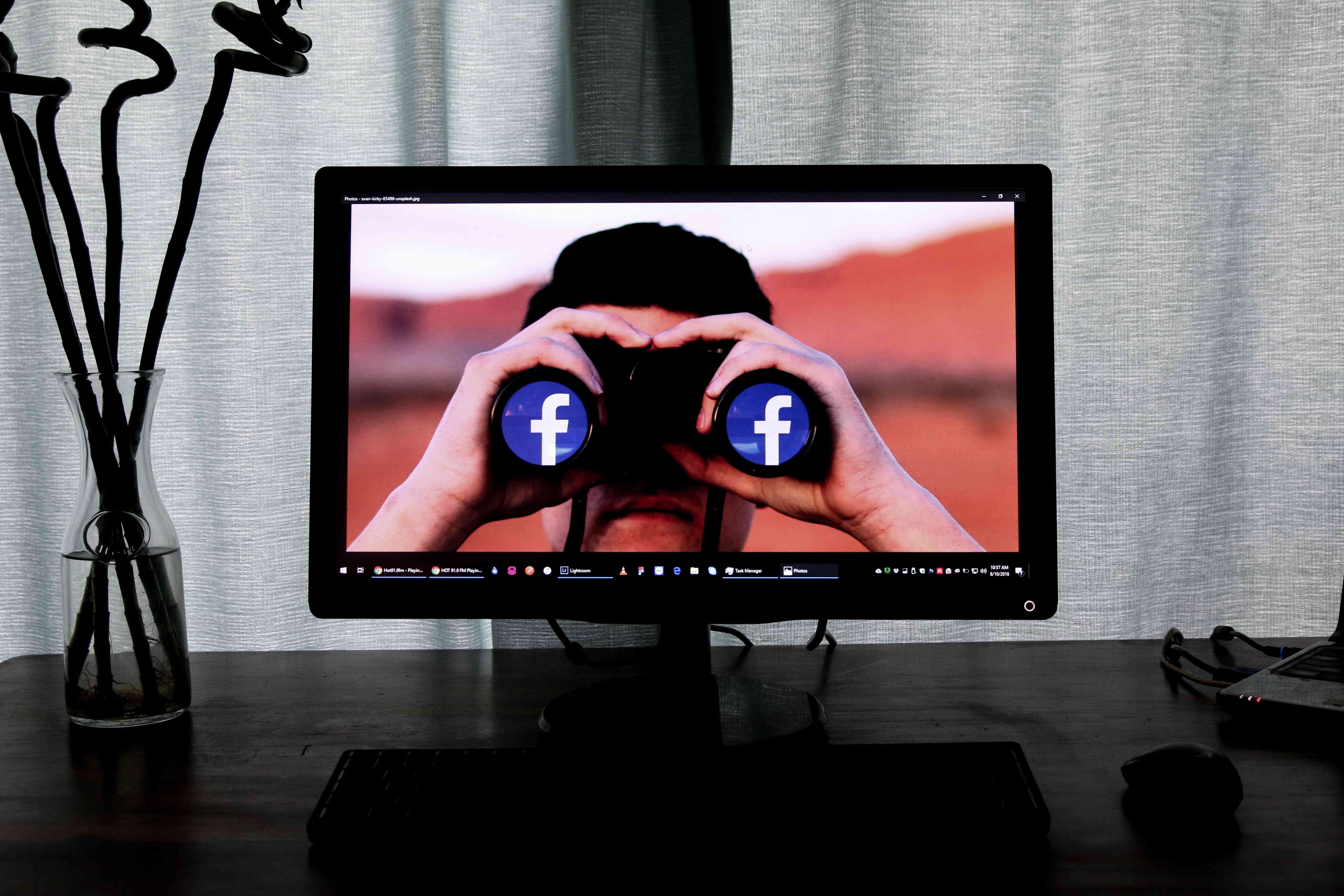 Een computerscherm met een afbeelding van een persoon die een verrekijker tegen zijn gezicht houdt met het Facebook-logo in plaats van lenzen.