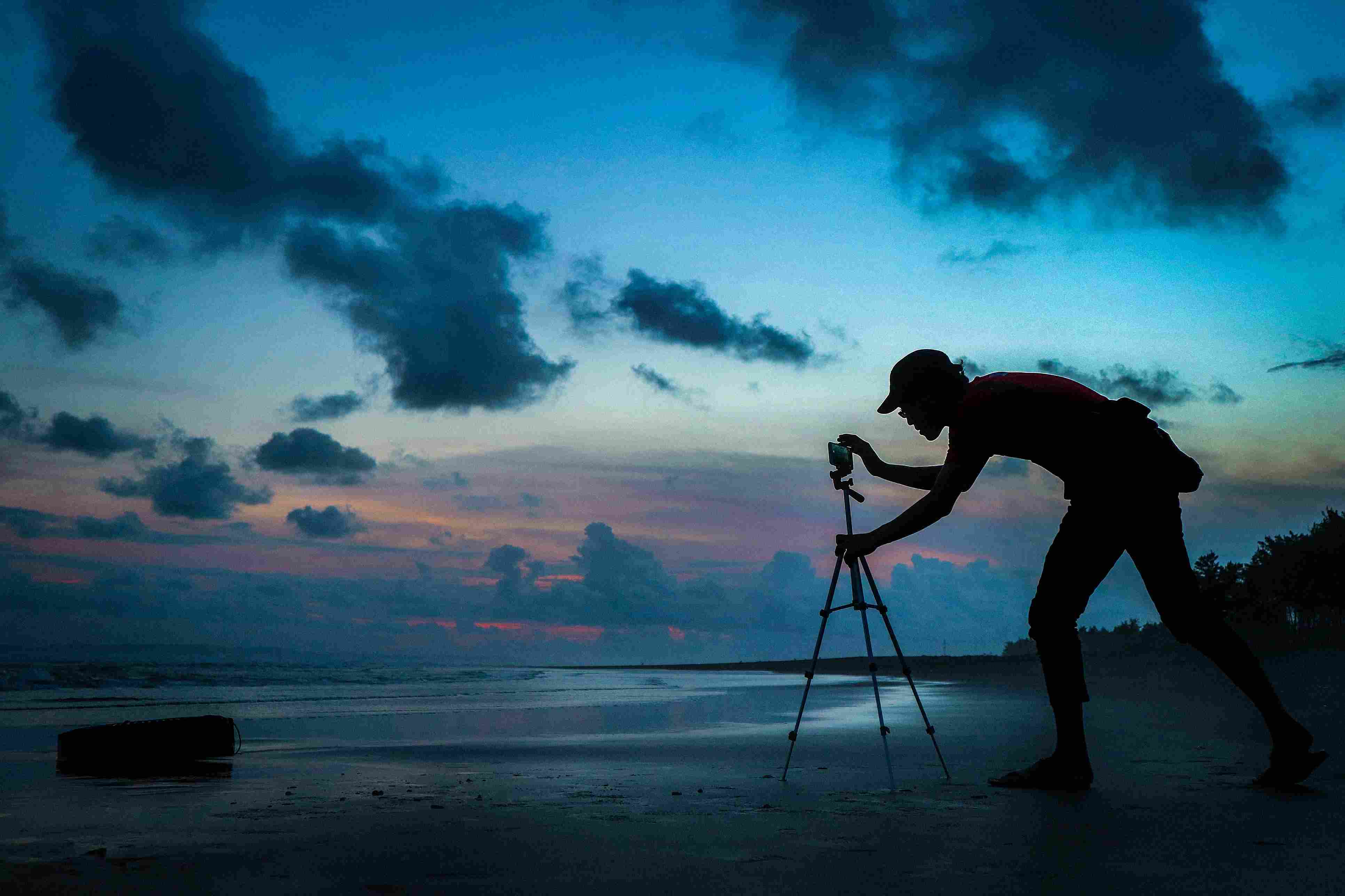 Silhouet man mobiele telefoon aan te passen op statief aan de kust tegen bewolkte hemel