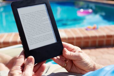 Een persoon in de buurt van een zwembad die een digitaal boek leest