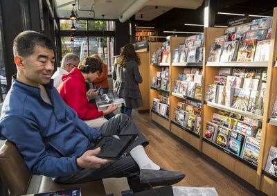 Persoon met e-reader, zittend naast tijdschriftenrek