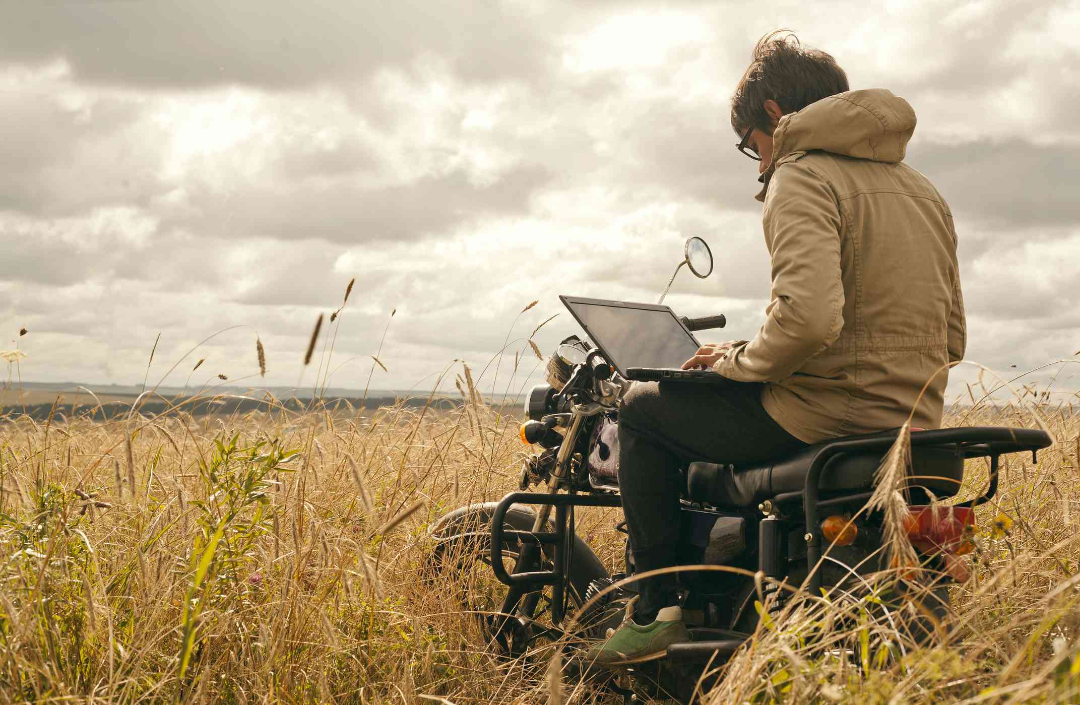 Iemand die een laptop gebruikt terwijl hij op een motor zit in het midden van een landelijk veld.