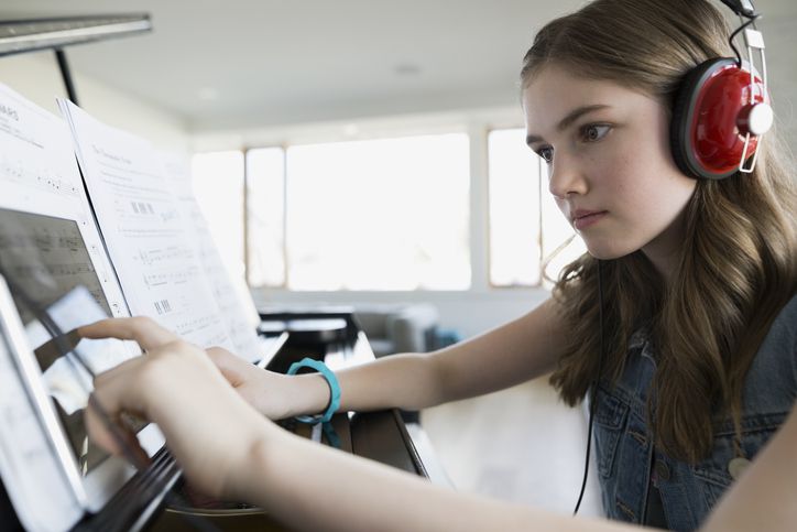 Geconcentreerd meisje met digitale tablethoofdtelefoons bij piano