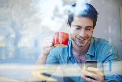 Man kijkt naar zijn telefoon in de etalage van een coffeeshop