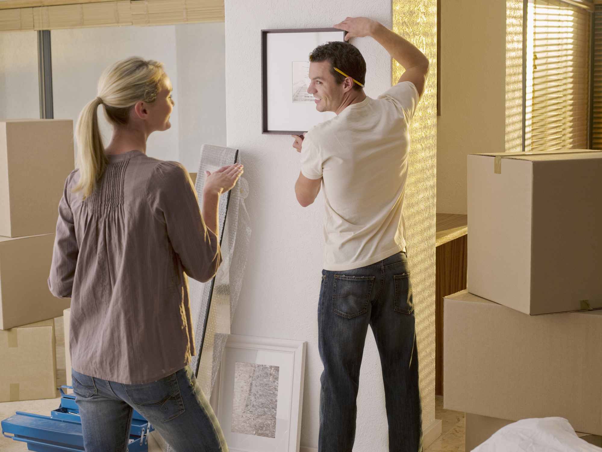 Man en vrouw hangen een schilderij aan de muur.