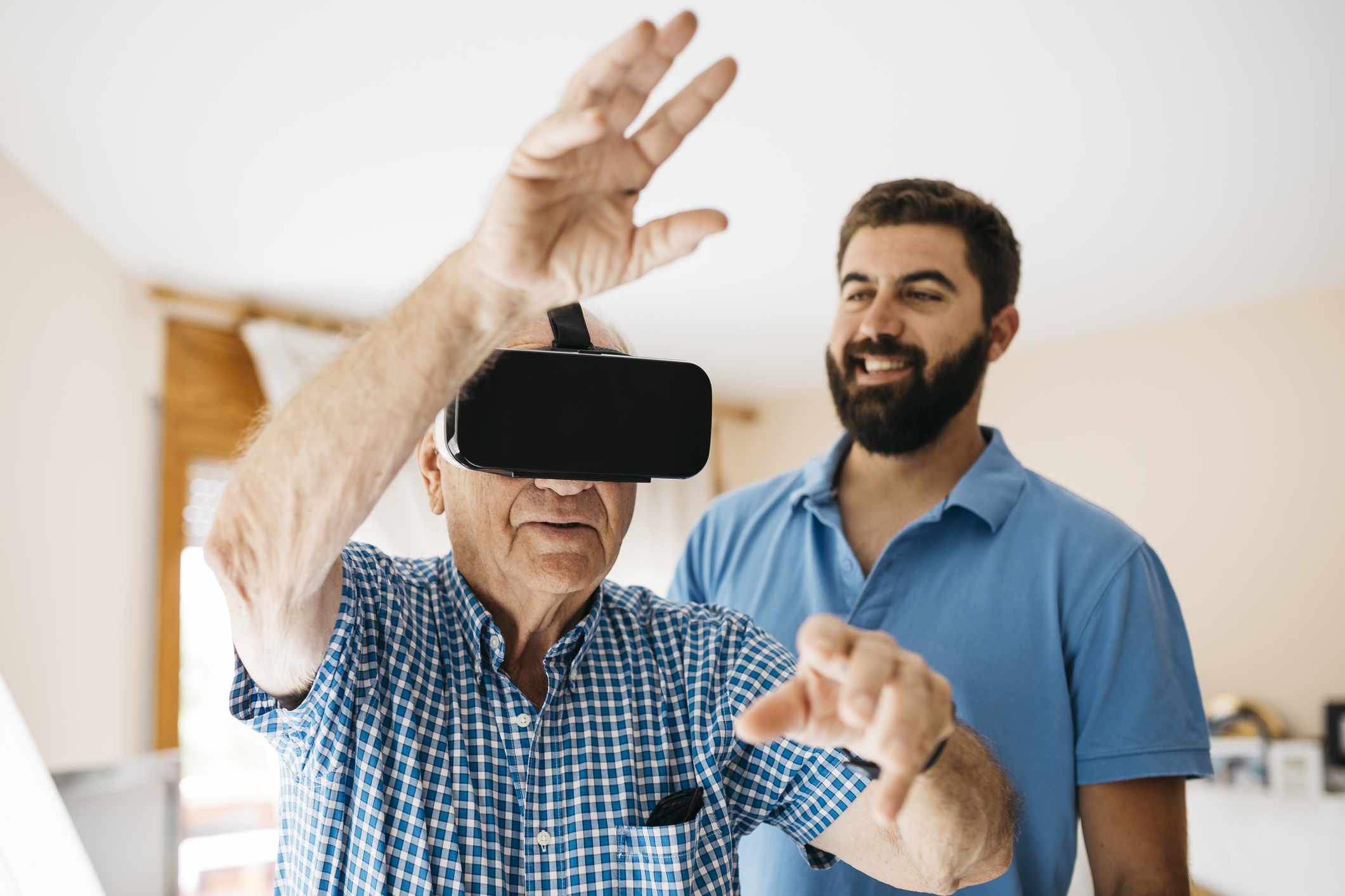 Senior man die thuis een virtual reality-bril gebruikt terwijl zijn volwassen kleinzoon naar hem kijkt