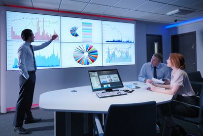 Drie zakenmensen bekijken gegevensgrafieken op een groot scherm