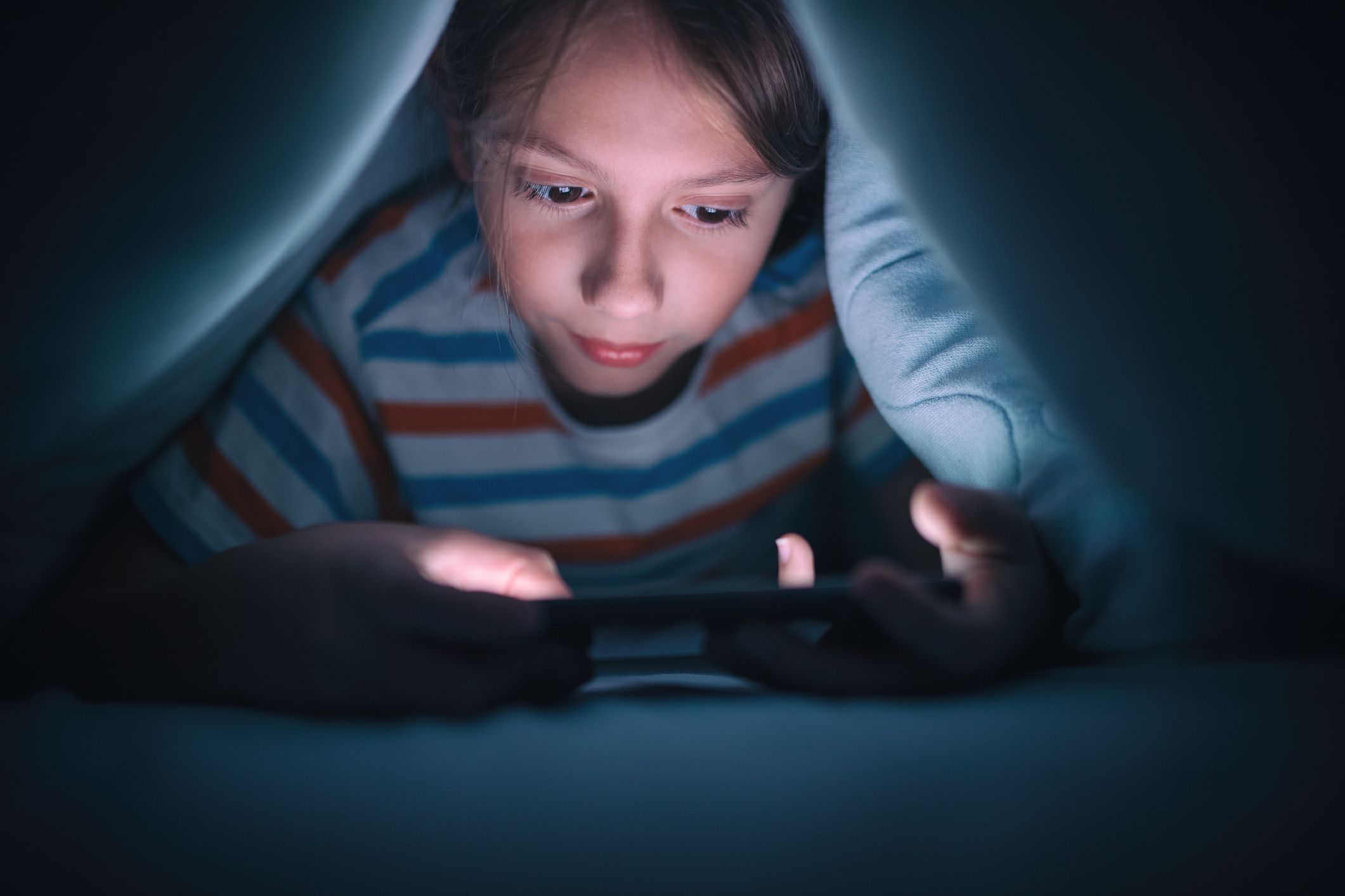 Een kind dat onder de dekens een handheld-videogame speelt. 