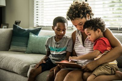 Een moeder en twee kinderen die een iPad op de bank gebruiken