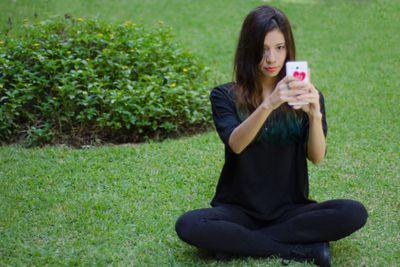 Jonge vrouw zittend op gras met behulp van een mobiele telefoon
