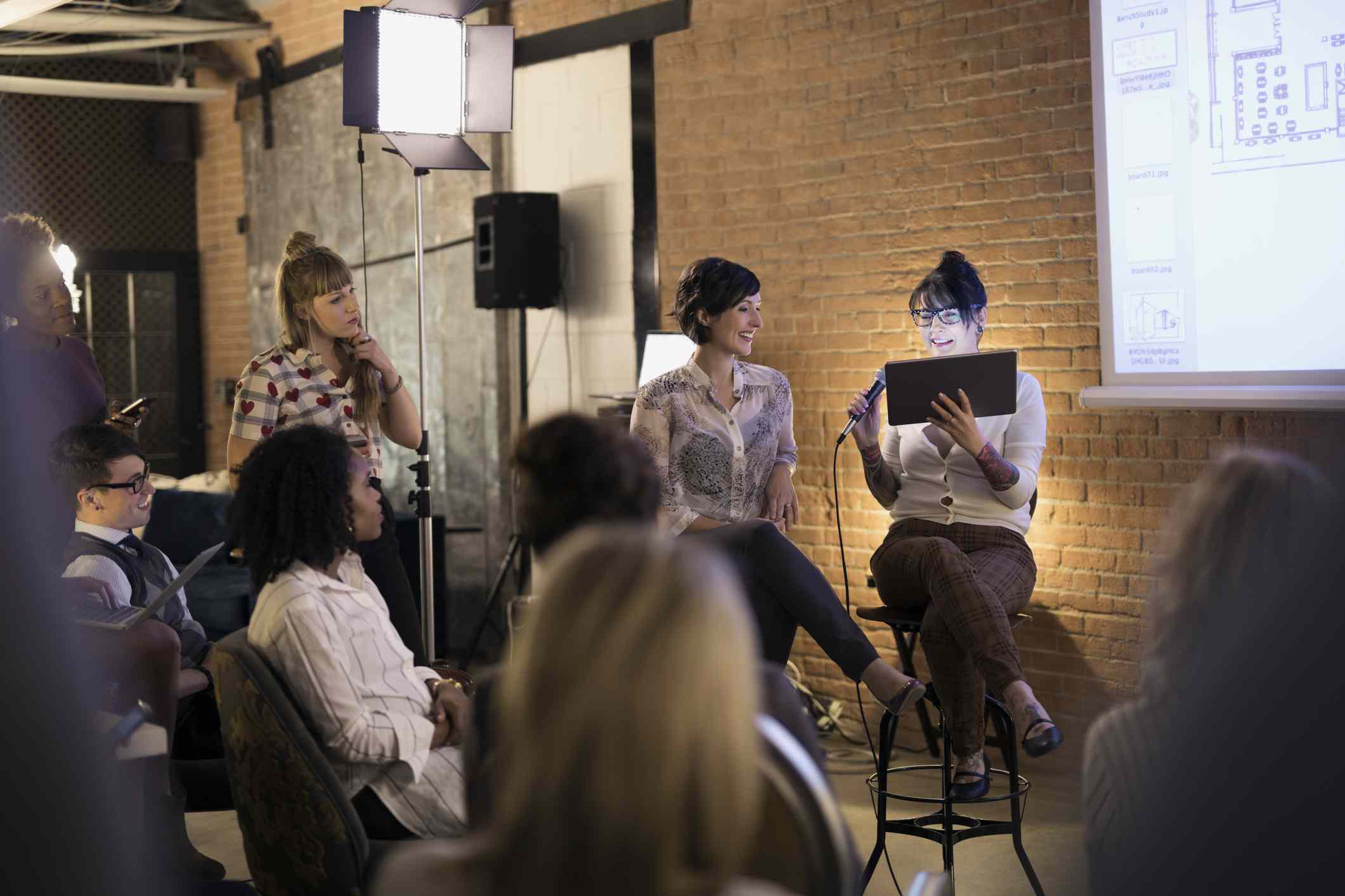 Vrouwelijke ontwerpers met microfoon en digitale tablet leidende conferentiebijeenkomst