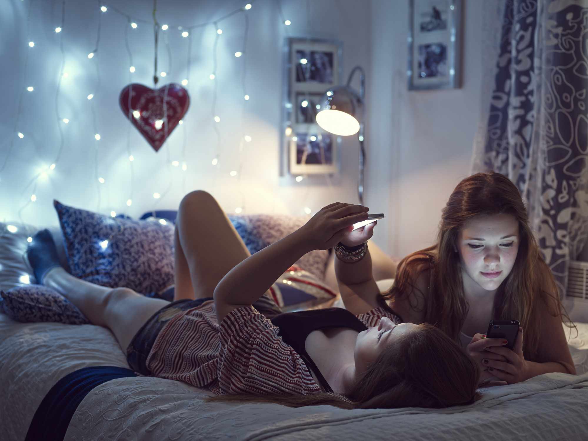 Twee jonge vrouwen die op een bed liggen.  Verlichting aan het voeteneinde van het bed.