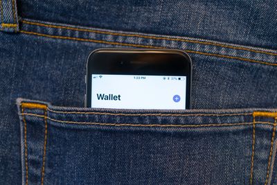 De Apple Wallet-app op een iPhone die uit de zak van een spijkerbroek steekt