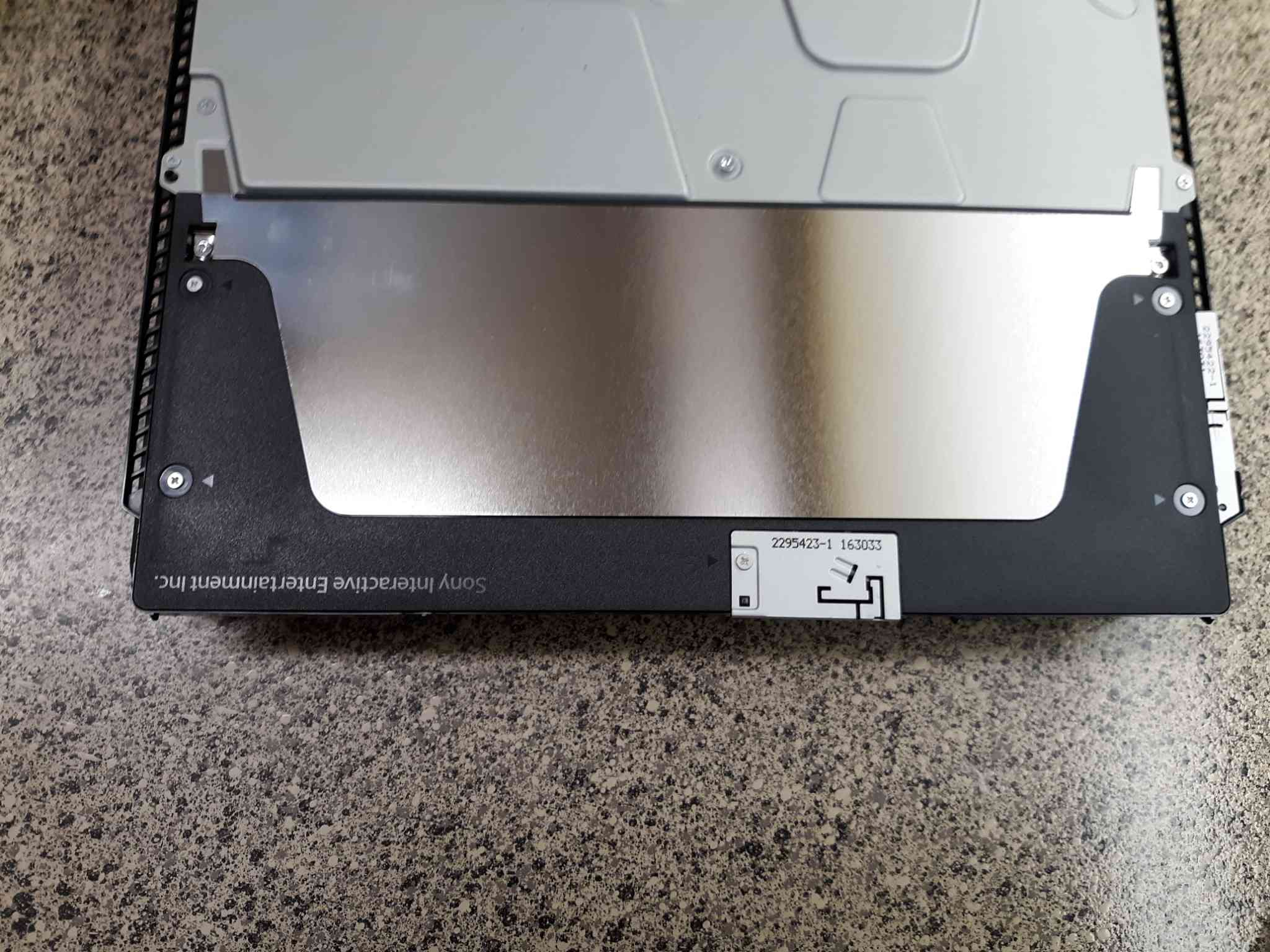 Gebruik een kruiskopschroevendraaier om de zwarte plastic afdekking aan de achterkant van de PS4-console te verwijderen.
